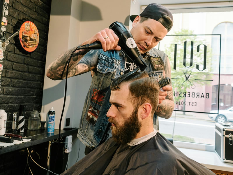Man getting a modern haircut at a barber shop, showcasing 2026 hair trends. Stylish male haircut being styled with a blow dryer.