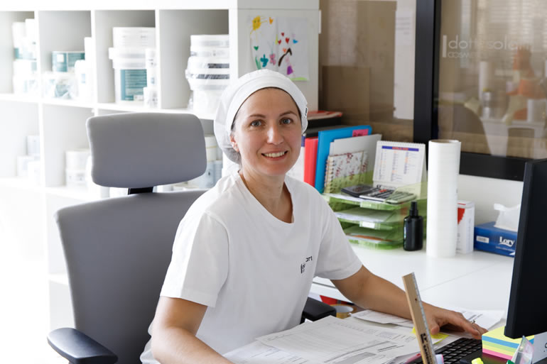 Dr. Claudia Solari, dentist staff member, smiling at her desk in the office. Professional dental staff portrait.