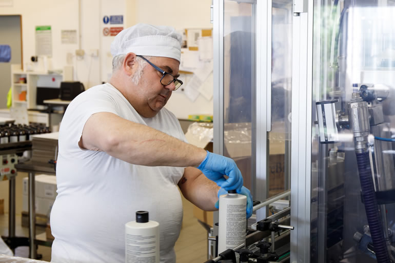 Dott. Solari Staff: Man in lab coat and gloves capping bottles on a production line, quality control in manufacturing.