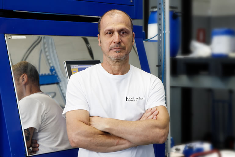 Dott. Solari Staff: Portrait of Raffaele, employee in white shirt, standing in front of industrial equipment. Cosmetics manufacturing.