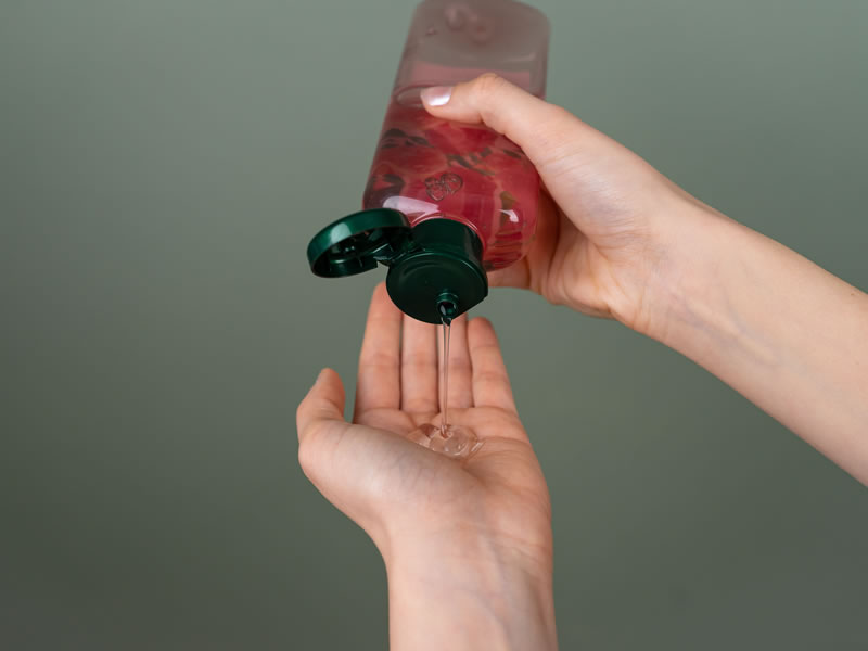 Hand pouring clear cosmetic gel from a translucent pink bottle with a green cap onto the palm.